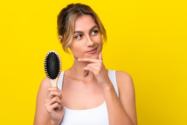 Junge uruguayische Frau mit Haarkamm isoliert auf gelbem Hintergrund, die eine Idee denkt und zur Seite schaut