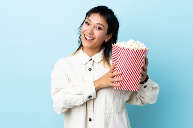 Junge uruguayische Frau über blauer Wand, die einen großen Eimer Popcorn hält