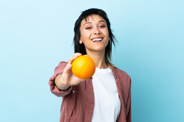 Junge uruguayische Frau über isoliertem Blau, das eine Orange hält