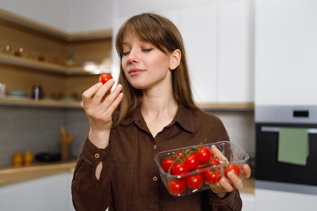 Junge vegane Frau untersucht Kirschtomaten, während sie in der Küche steht