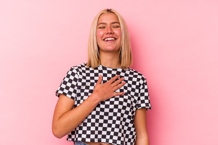 Foto junge venezolanische frau, die auf rosa wand isoliert wird, lacht laut und hält hand auf brust.