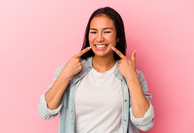 Junge venezolanische Frau isoliert auf rosa Hintergrund lächelt und zeigt mit dem Finger auf den Mund