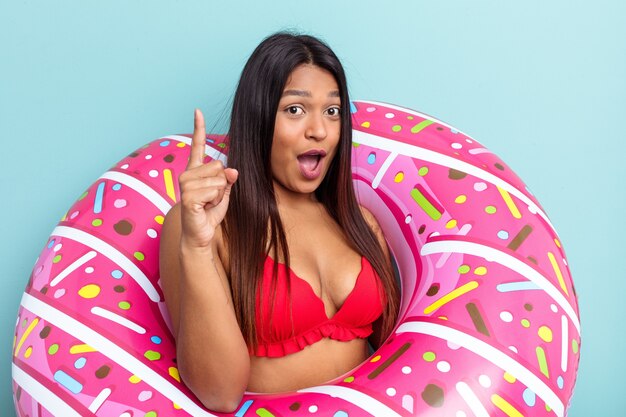 Junge venezolanische Frau mit aufblasbarem Donut isoliert auf blauem Hintergrund mit einer Idee, Inspirationskonzept.