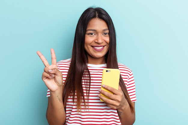 Junge venezolanische Frau mit Handy auf blauem Hintergrund isoliert zeigt Nummer zwei mit den Fingern.