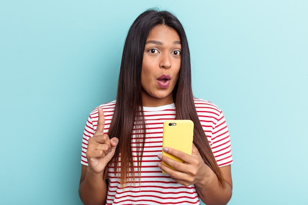 Junge venezolanische Frau mit Handy isoliert auf blauem Hintergrund mit einer großartigen Idee, Konzept der Kreativität.