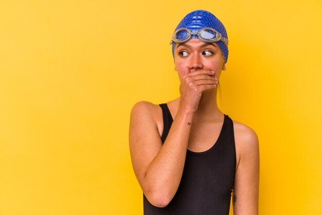 Foto junge venezolanische schwimmerin isoliert auf gelbem hintergrund nachdenklich auf der suche nach einem kopienraum, der den mund mit der hand bedeckt.