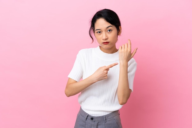 Junge vietnamesische Frau isoliert auf rosa Hintergrund, die die Geste der Verspätung macht