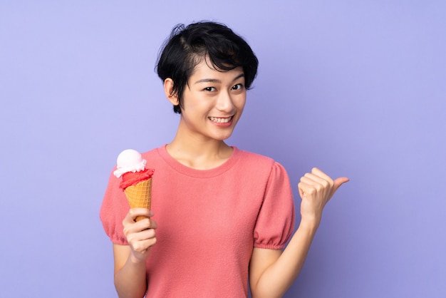 Junge vietnamesische Frau mit kurzen Haaren, die ein Kornetteis über lila Wand hält, die zur Seite zeigt