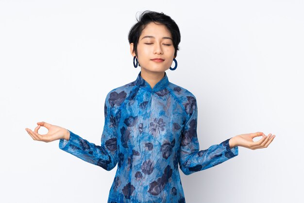 Junge vietnamesische Frau mit kurzen Haaren, die ein traditionelles Kleid über isoliertem Weiß in Zen-Pose tragen