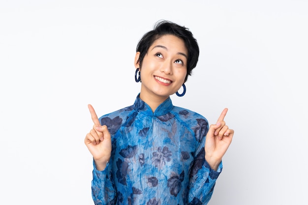 Junge vietnamesische Frau mit kurzen Haaren, die ein traditionelles Kleid über weißer Wand tragen, die eine große Idee aufzeigt