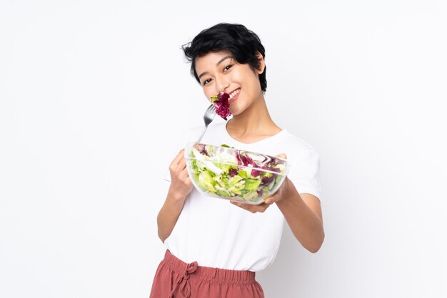 Junge vietnamesische Frau mit kurzen Haaren, die einen Salat über Wand halten