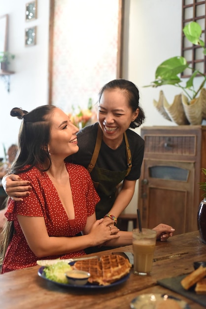 Junge vietnamesische Kellnerin lächelt und umarmt einen befreundeten Kunden