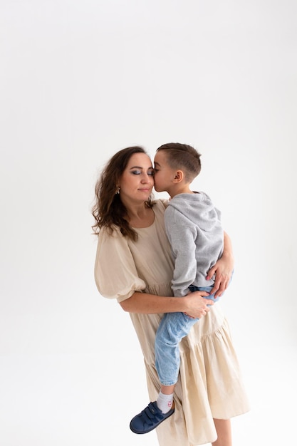 Junge Vorschüler und Mutter lächeln und umarmen auf grauem Hintergrund im Fotostudio