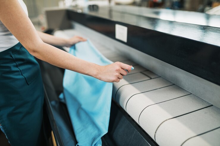 Junge Wäscherei-Arbeiter klopfen die Wäsche auf dem Automaten in der chemischen Reinigung.