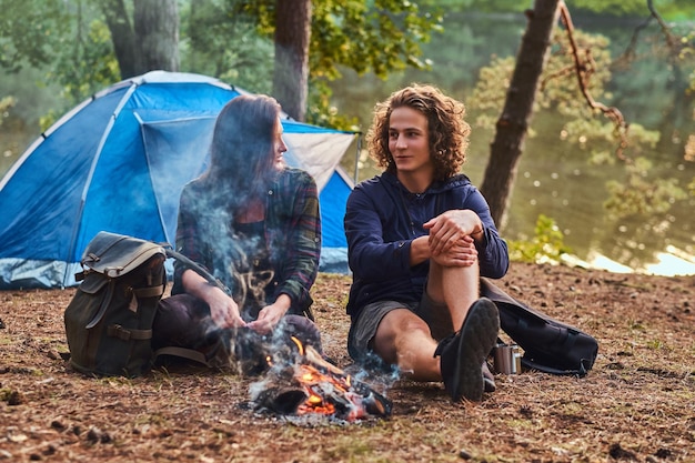 Junge Wanderer sitzen und unterhalten sich, während sie sich am Lagerfeuer im Wald aufwärmen.