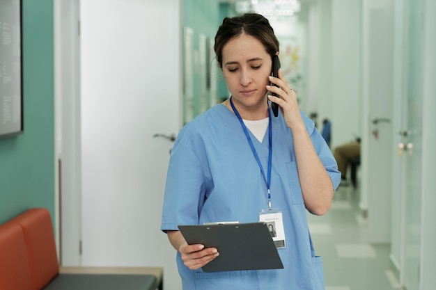 Junge weibliche Assistentin in blauer Uniform, die den Patienten per Handy berät