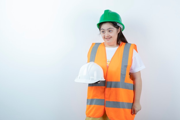 Junge weibliche Bauarbeiterin im Helm, der Helme über weißer Wand hält.