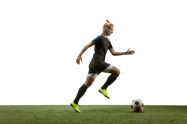 Junge weibliche Fußball- oder Fußballspielerin mit langen Haaren in Sportbekleidung und Stiefeln, die den Ball für das Ziel im Sprung auf weißem Hintergrund treten. Konzept eines gesunden Lebensstils, Profisport, Bewegung, Bewegung.