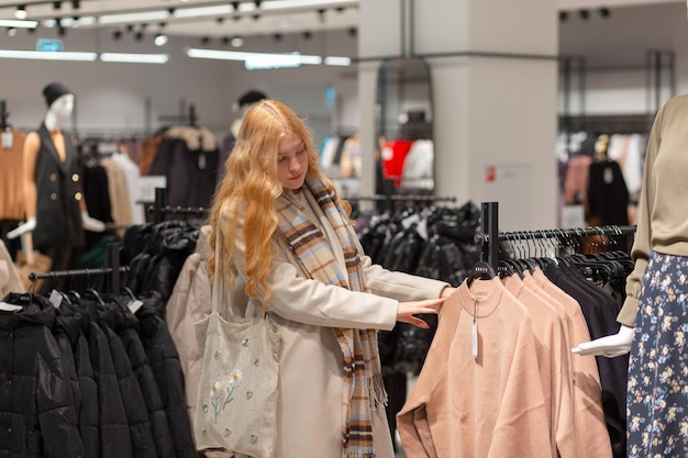 Junge weibliche Kundin mit goldenem Haar, die Kleidung im modernen Damentuchladen auswählt