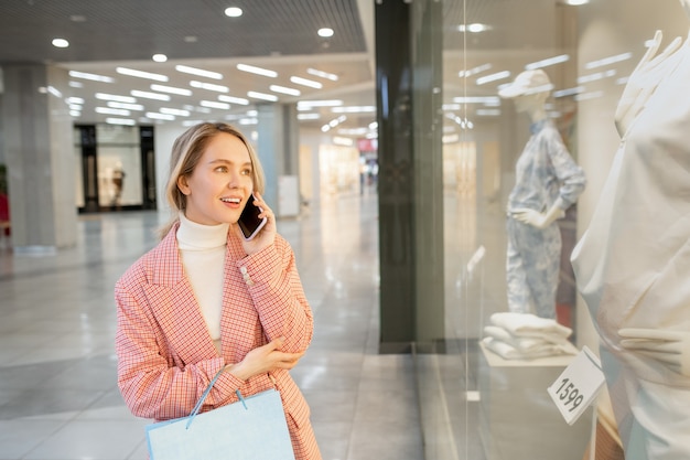 Junge weibliche Shopaholic, die über ein großes Display telefoniert