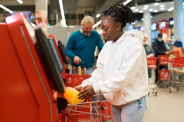 Junge weibliche Verbraucher scannen eine Flasche Saft, während sie ein Selbstbedienungsterminal verwenden