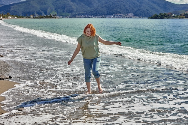 Junge weiße Frau geht barfuß auf Sand in Surfline am Strand im Ferienort Fethiye im zeitigen Frühjahr