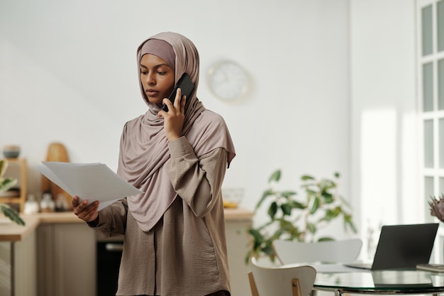 Junge Wirtschaftswissenschaftlerin im Hijab, die einen Geschäftsvertrag durchsucht und mit einer Kollegin spricht