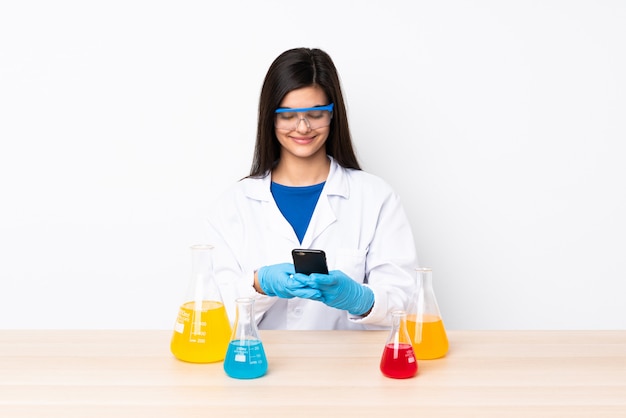 Junge wissenschaftliche Frau in einer Tabelle, die eine Nachricht mit dem Handy sendet