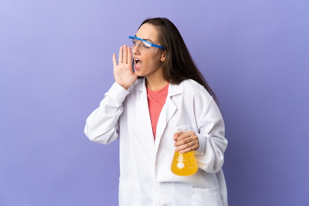 Junge wissenschaftliche Frau über isolierter Wand, die mit dem Mund weit offen zur Seite schreit