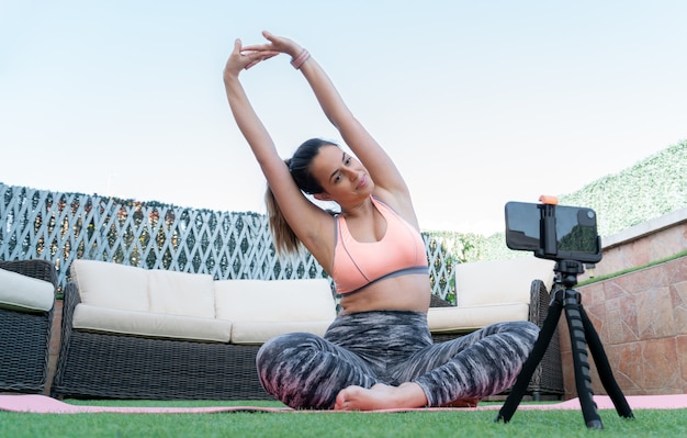 Junge Yogalehrerin, die eine Online-Klasse mit ihrem Handy im Garten ihres Hauses aufzeichnet