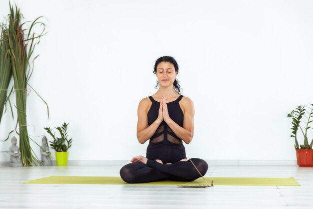 Foto junge yogi-frau meditiert mit einem rauchenden aromastick, während sie in einem yoga-studio auf einer matte sitzt