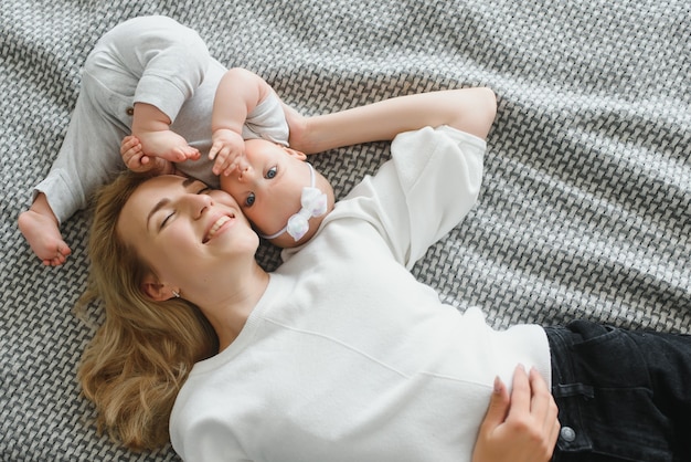 Junge zarte glückliche Mutter, die ihr neugeborenes Baby lächelnd am Morgen auf dem Bett sitzend umarmt