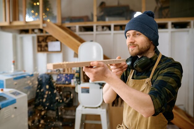 Foto junge zimmermann bläst sägemüll von einer holzplatte aus holzbearbeitung im modernen tischlerstudio