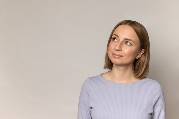 Junge zufällige Frau tausendjähriger Blick weg zur Seite mit neugierigem Lächeln zur leeren Ecke über Studiowand