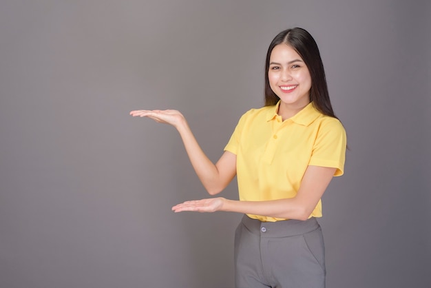 Junge zuversichtliche schöne Frau, die gelbes Hemd trägt, ist auf grauem Hintergrundstudio