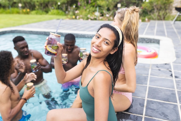 Junge, zweirassige Frau in einem grünen Badeanzug genießt eine Poolparty mit Freunden