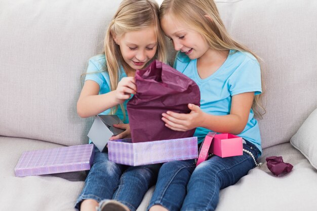Junge Zwillinge, die das Geburtstagsgeschenk auspackt, das auf einer Couch sitzt