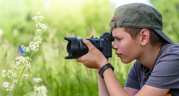 Junge, zwölf Jahre alt, schießt blauen Schmetterling auf die wilde Blume in der Natur am Sommertag