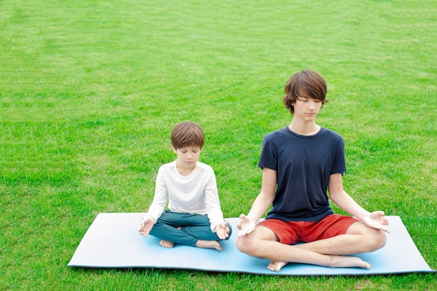 Jungen, die draußen Yoga auf dem grünen Gras tun