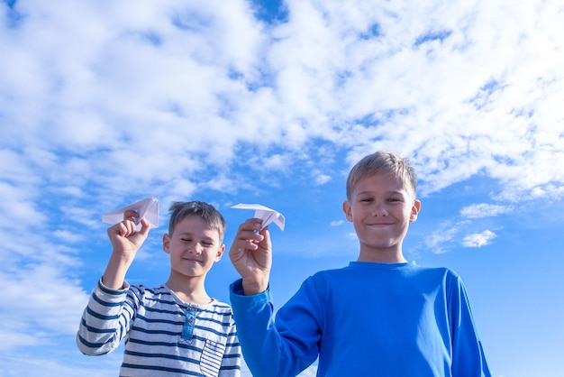 Foto jungen halten ein papierflugzeug, während sie gegen den himmel stehen