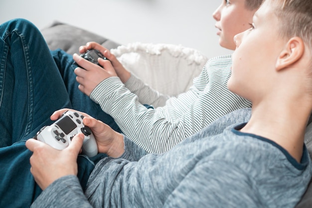 Jungen im Schulalter sitzen auf dem Sofa mit Spiel-Joysticks Seitenansicht von oben Kinder spielen Videospiele Interessante Unterhaltung