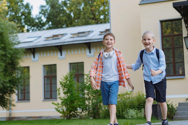 Jungen laufen an einem sonnigen Tag mit Rucksäcken vor der Haustür der Schule zu Beginn des Schuljahres