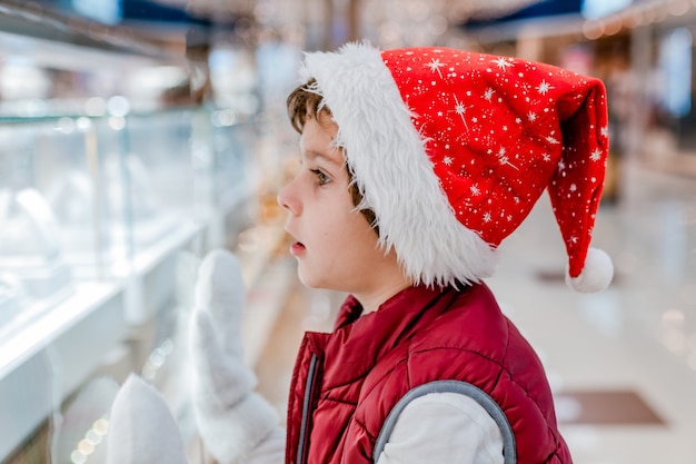 Jungen mit Weihnachtsmütze schaut durch das Fenster auf dem Markt in den Laden