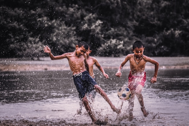 Jungen spielen Fußball auf einem schlammigen Wasser