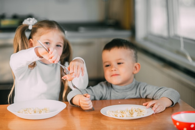 Jungen und Mädchen in der Küche, die Würstchen mit Nudeln essen, sind sehr lustig und freundlich, sehr süß