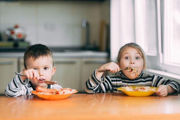 Jungen und Mädchen in der Küche essen Nudeln sehr hungrig