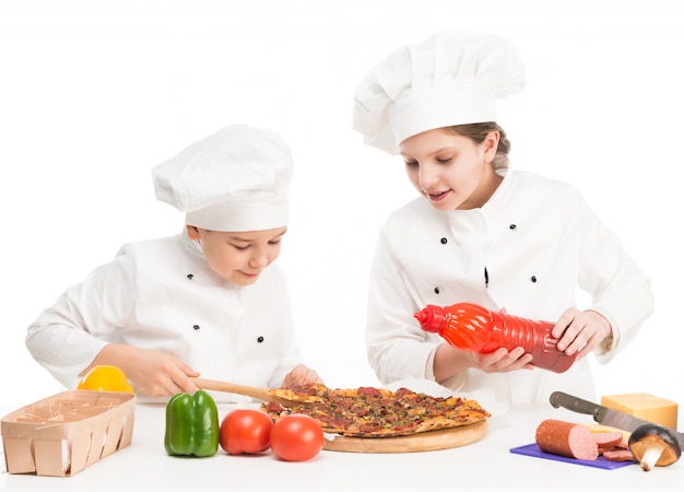 Jungen und Mädchen in weißer Uniform am Tisch mit Pizza