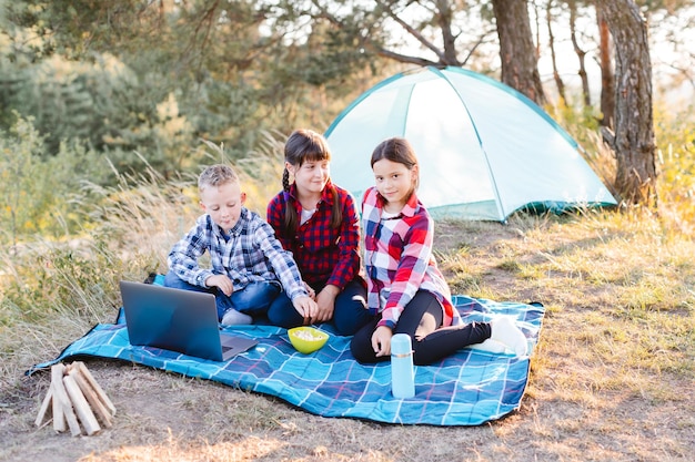 Jungen und Mädchen ruhen sich in einem Zeltlager aus Kinder sitzen im Sommer auf dem Plaid auf dem Rasen