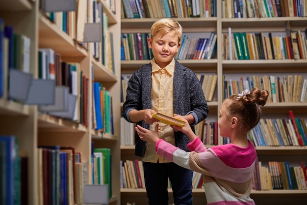 Jungen und Mädchen unterhalten sich in der Bibliothek, diskutieren über Bücher und wählen Bücher für die Schule aus. zwischen Bücherregalen stehen