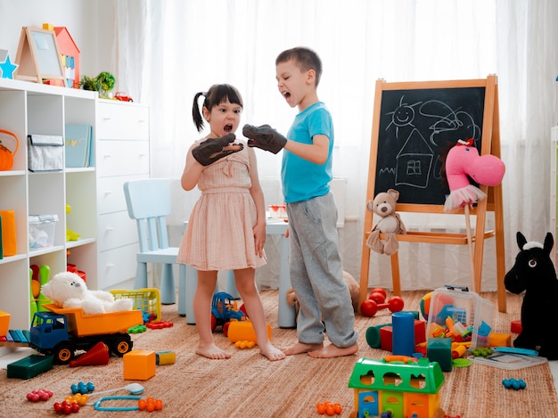 Jungen- und Mädchenkinder, die mit Spielzeugdinosauriern schreien und im Kinderzimmer spielen.